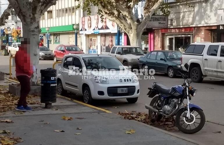 Los dos en infracción. No solo la moto está mal estacionada sino que el auto de la imagen está en línea amarilla.